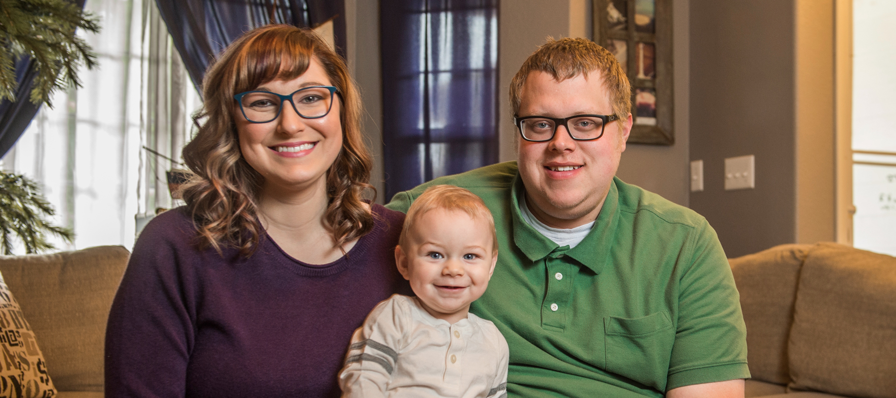 A woman, a man, and a child sitting on a couch smiling for the camera. 