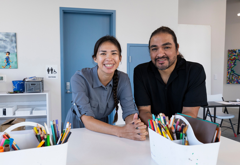 Two people leaning on a table of art supplies