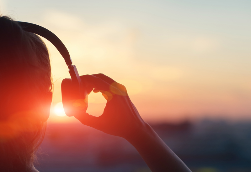 A person holding headphone away from their ear while watching the sunset