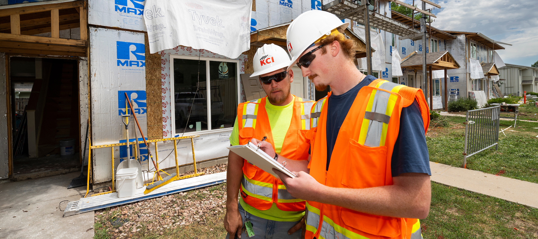 Two men in orange safety vests in front of construction