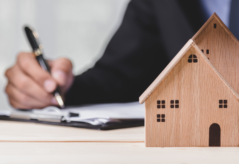 A person at a desk writing on paper with small wooden houses next to the paper