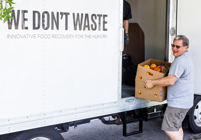 A person loading a box of produce onto a truck that reads We Don't Waste