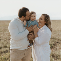 A mother and father in white kissing their baby